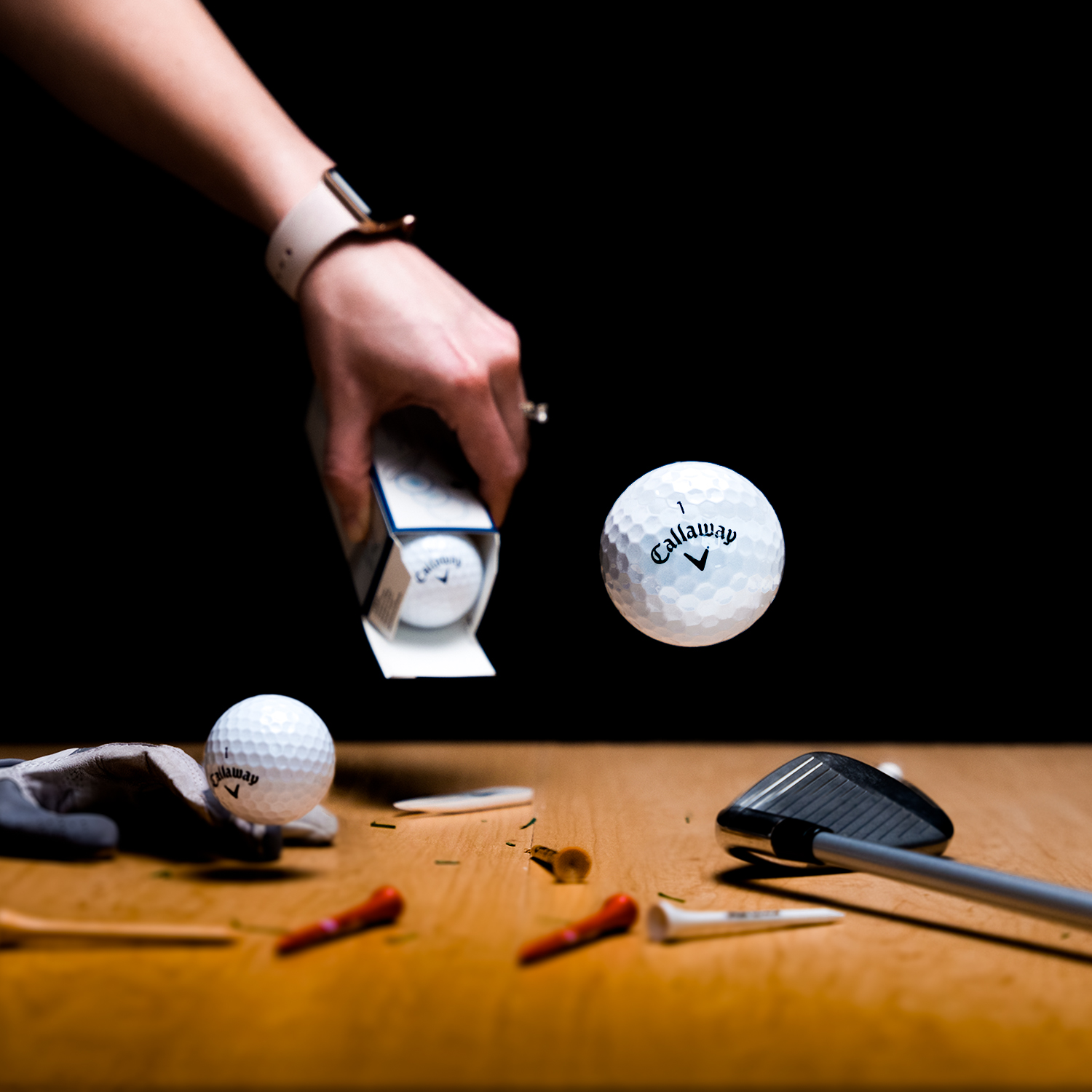 A box of golf balls being opened onto a wooden surface